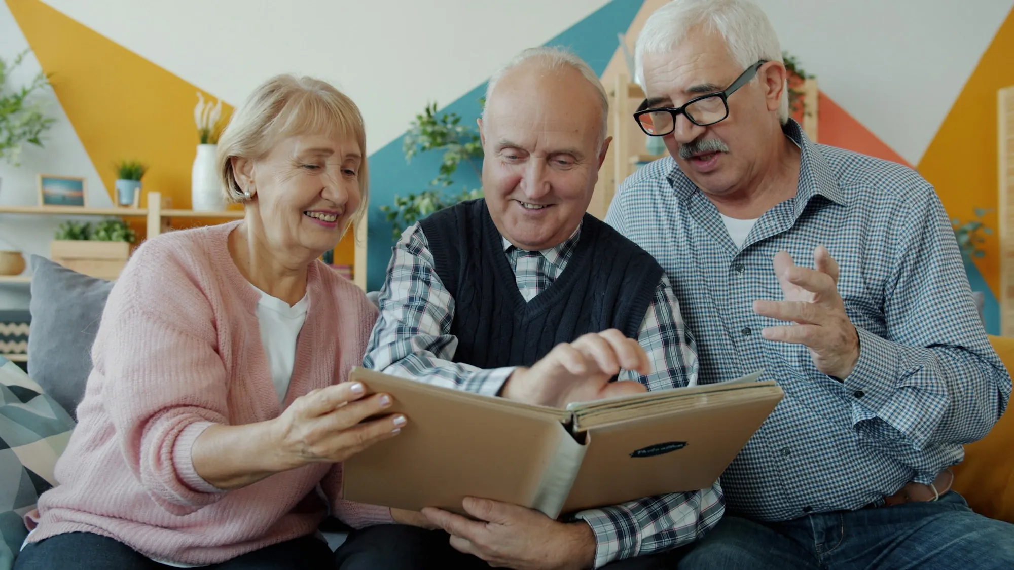 Three older adults looking through a photo album together over tea