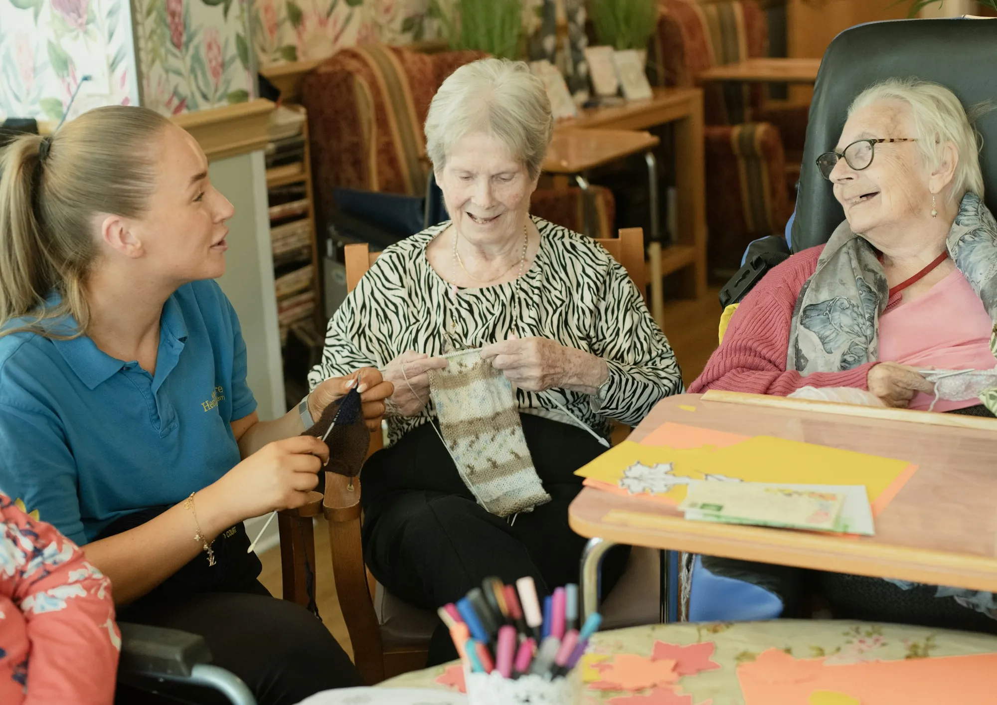 A caregiver sitting with two older women over a shared knitting project