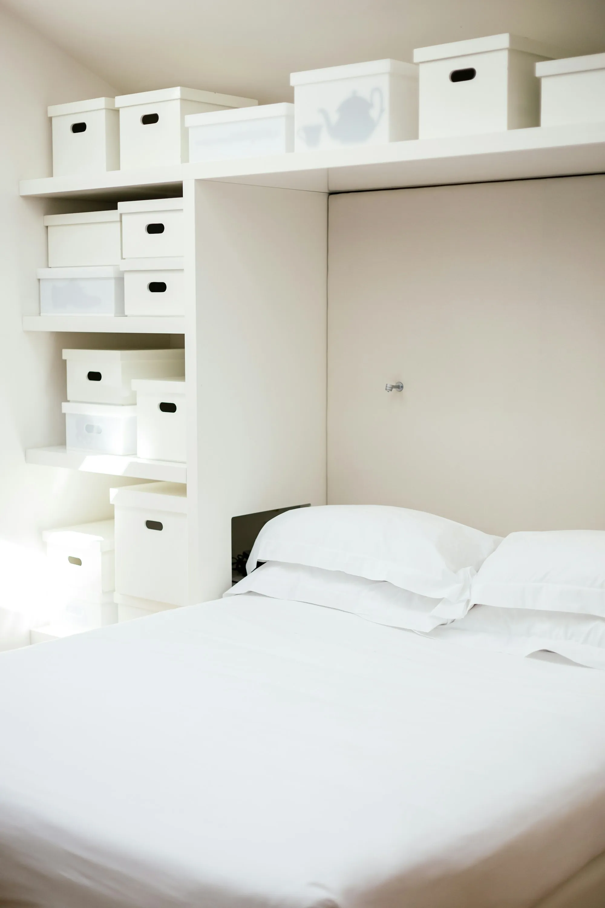 Fresh white bed linen on a made bed beside a wooden cabinet