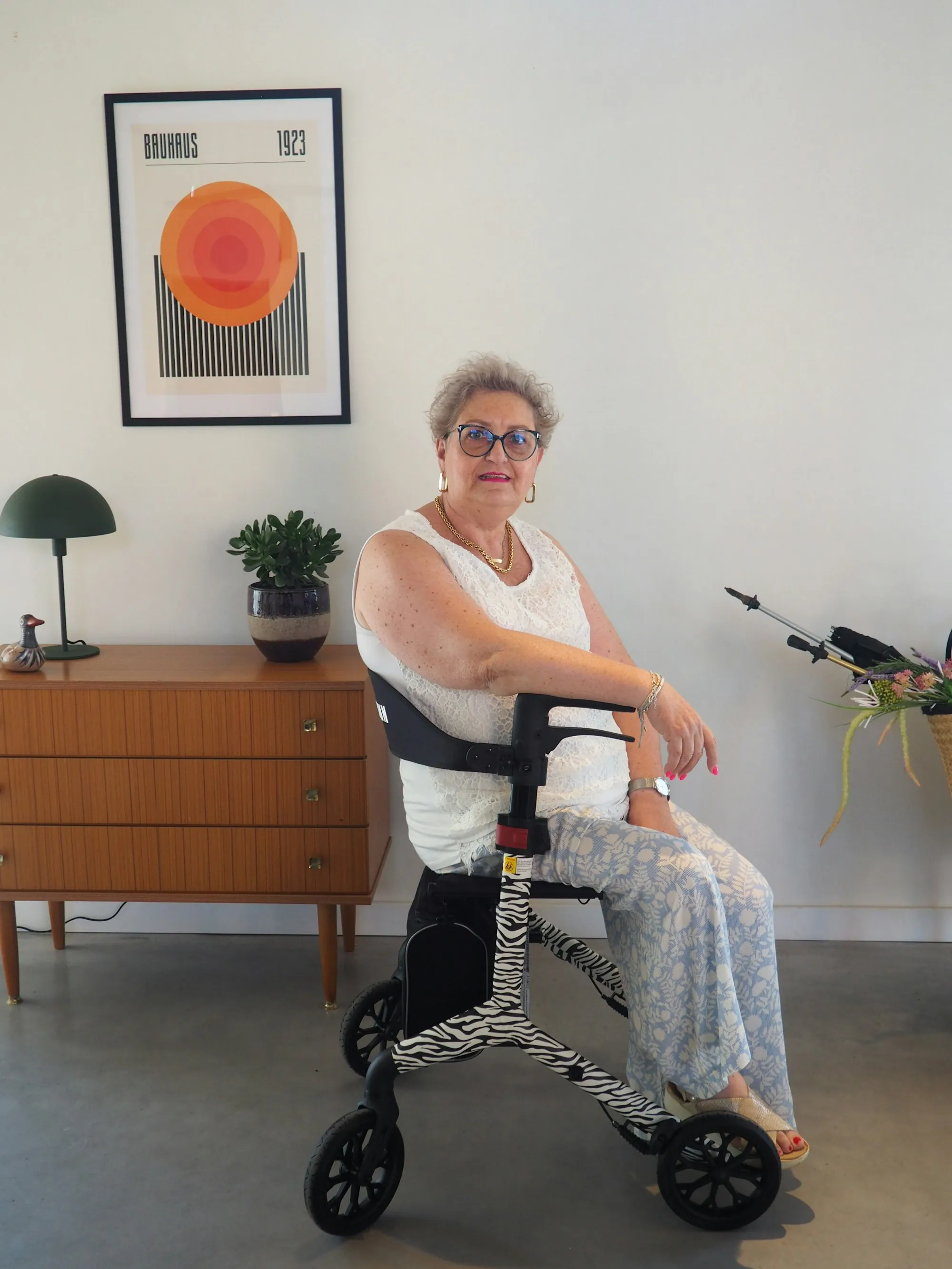 An older woman seated on a wheeled walker indoors, smiling