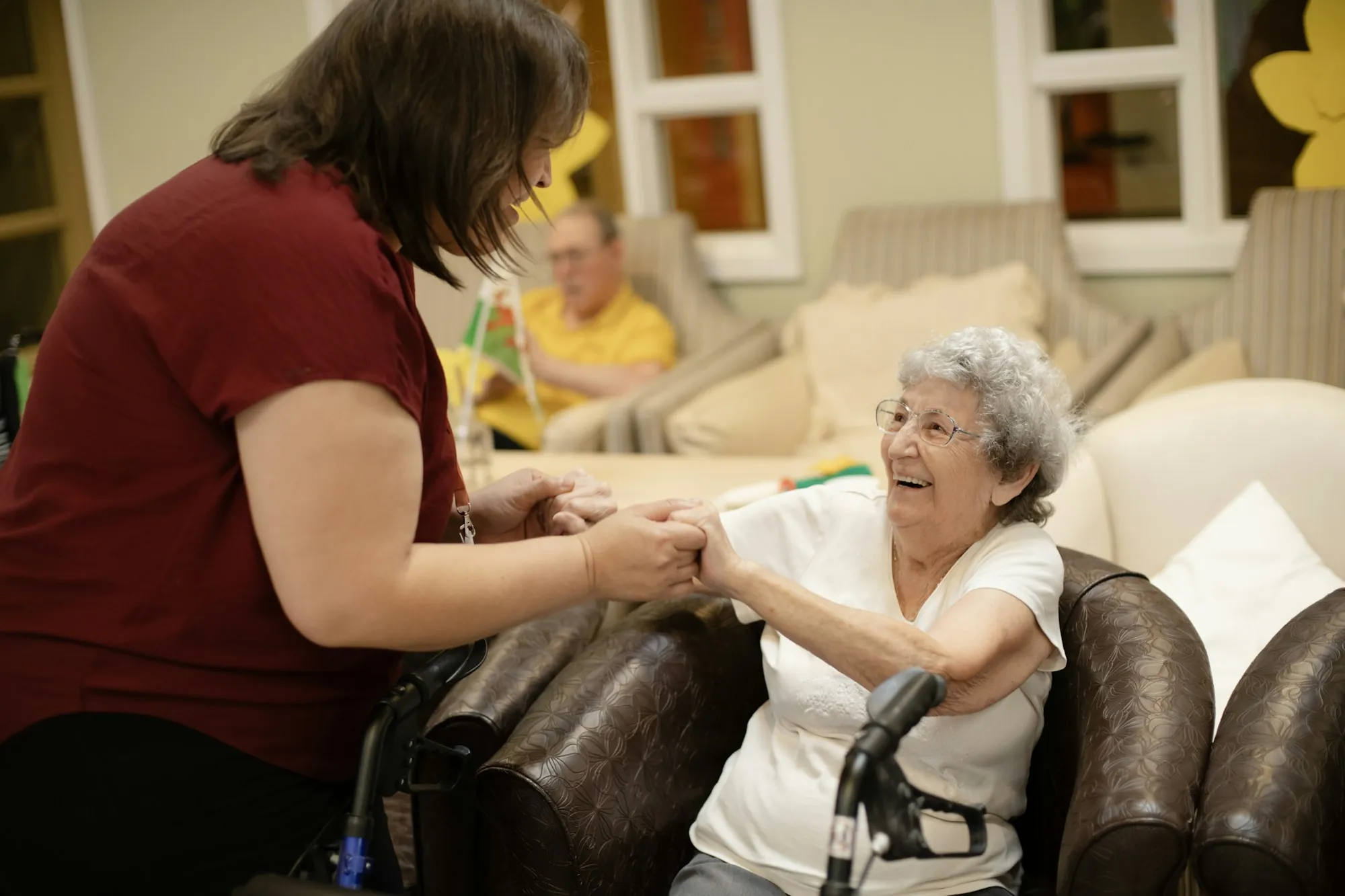 A caregiver steadying an older woman as she walks with a wheeled walker